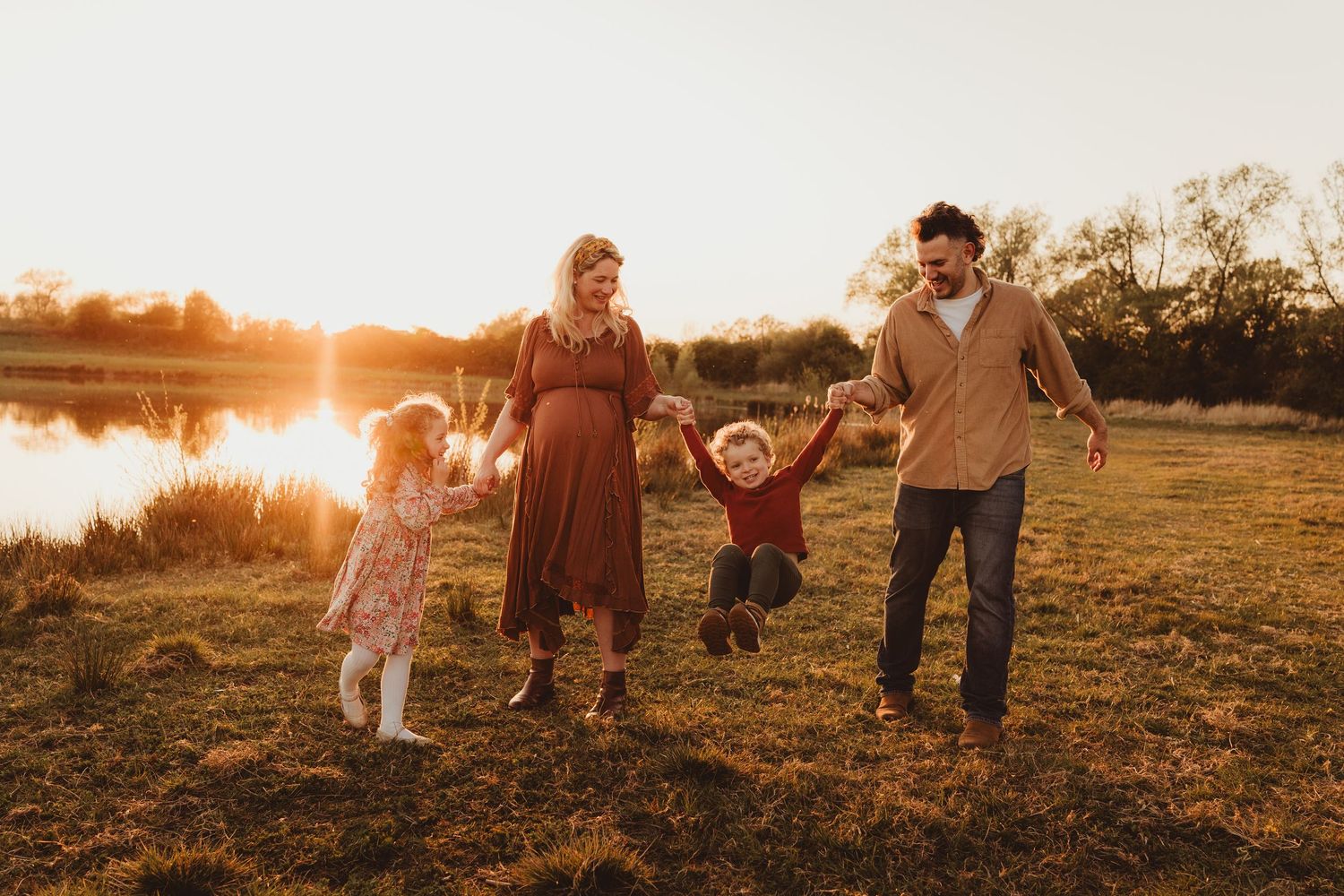 A family plays together in a grassy field at sunset near a serene lake in Gloucestershire.