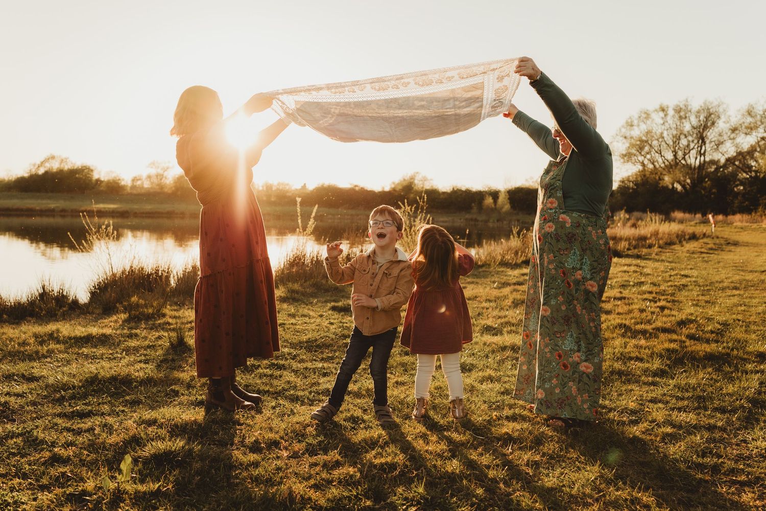 A family plays together in a grassy field at sunset near a serene lake in Gloucestershire.