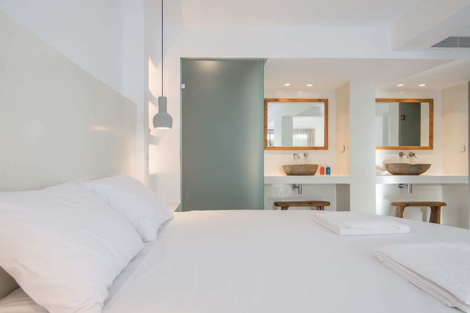 Serene hotel bedroom with ensuite bathroom featuring wooden mirror frames and modern fixtures.