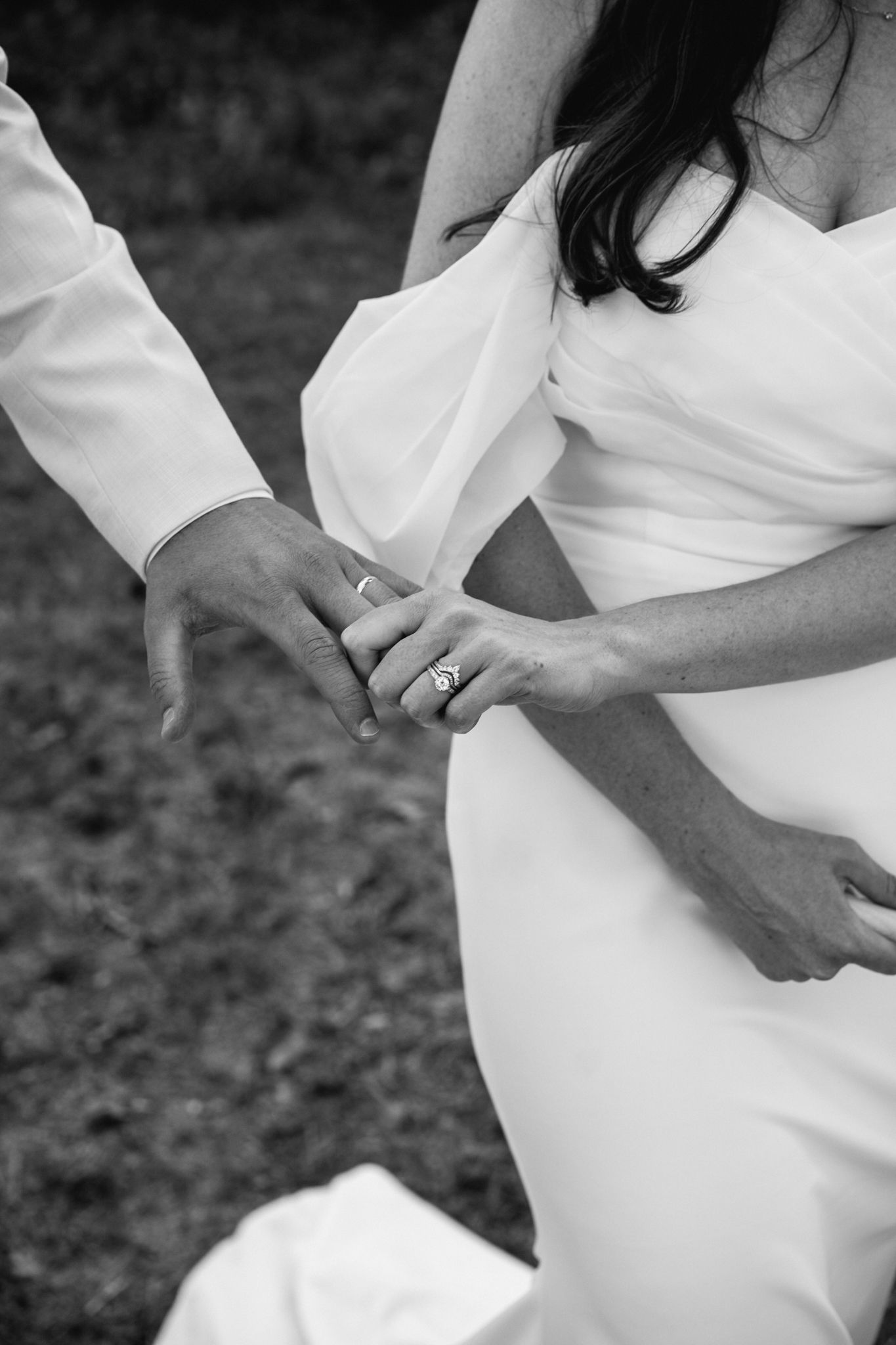 Black and white close-up of bride and groom holding hands showing wedding ring during ceremony.