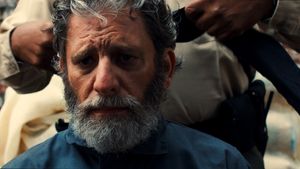Man with gray beard getting a haircut in a dimly lit room.