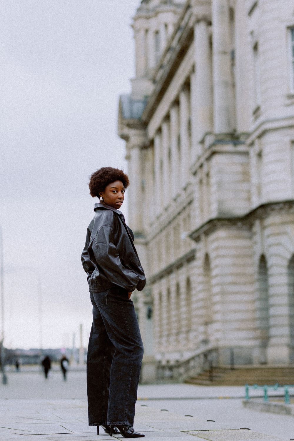 A series of photos showing a person in a black jacket standing against a white stone building.