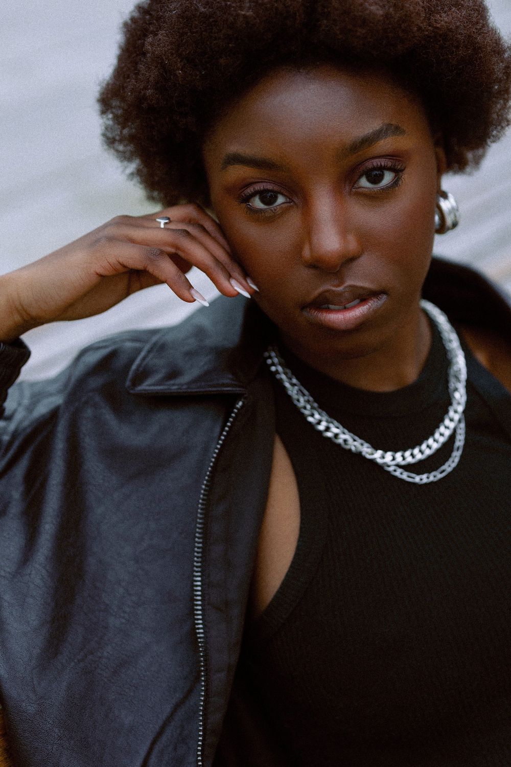 Portrait series showing a person wearing a black jacket and silver chain necklace in various poses against a light background.