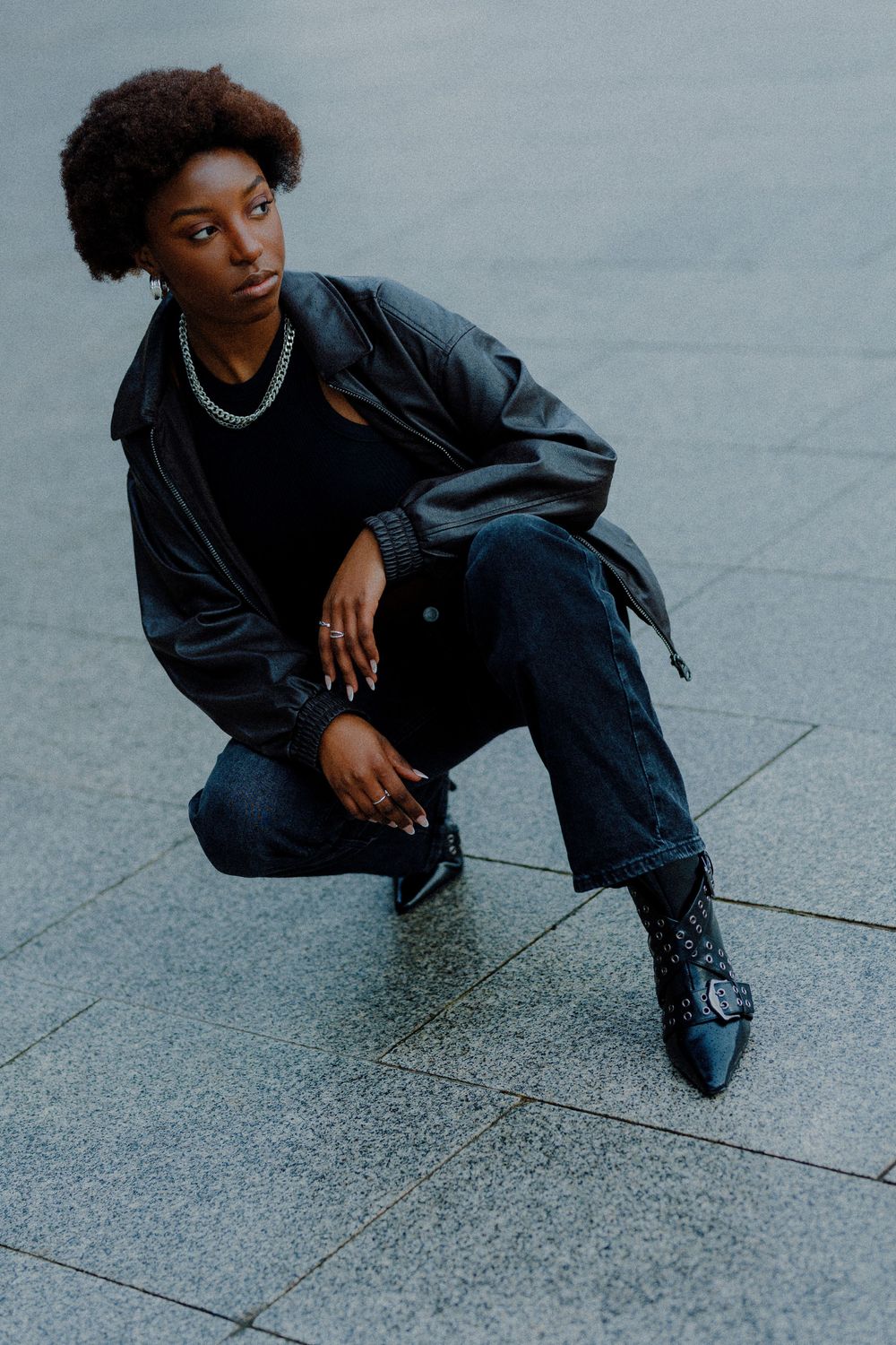 Urban fashion photography with model in dark denim crouching on concrete ground.