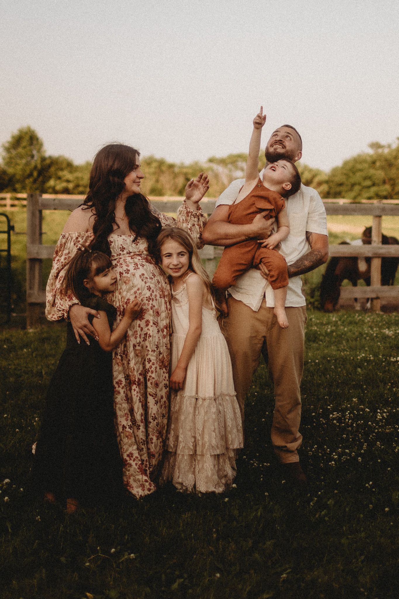 Family poses playfully together in a grassy field during golden hour sunset photography session.