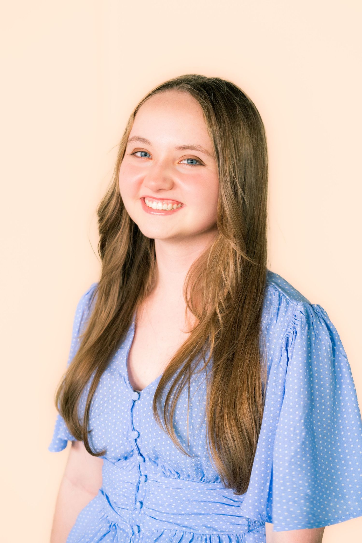 A person wearing a light blue polka dot dress with flutter sleeves poses against a beige background.