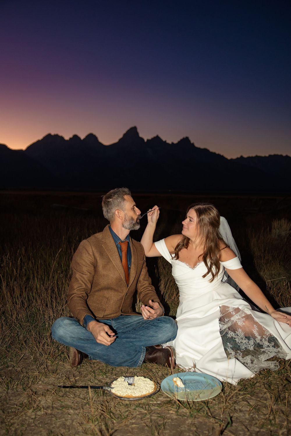 Bride and groom eat wedding cake at sunset in Grand Teton National park