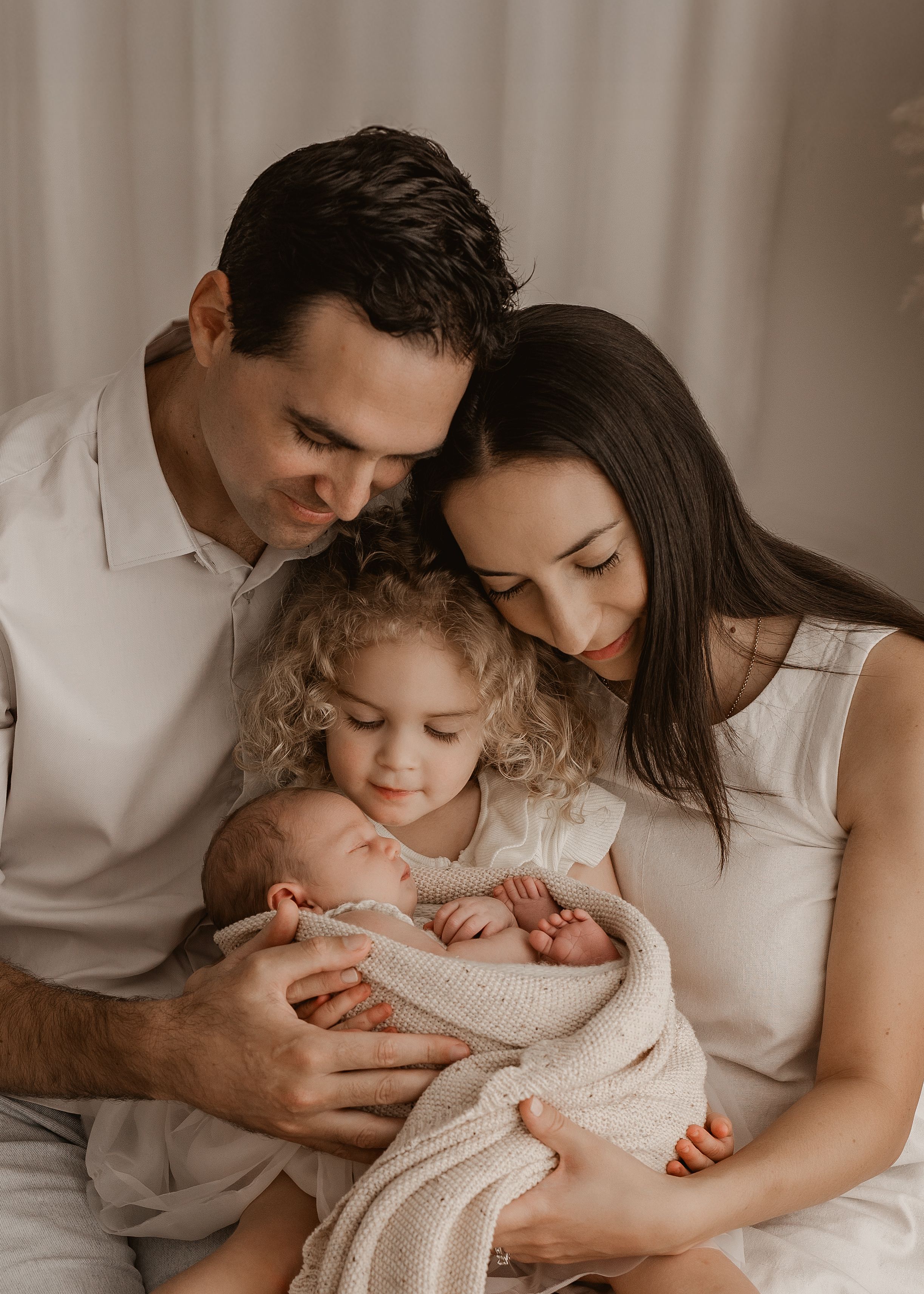 Intimate family moment with parents cradling young child in white room.