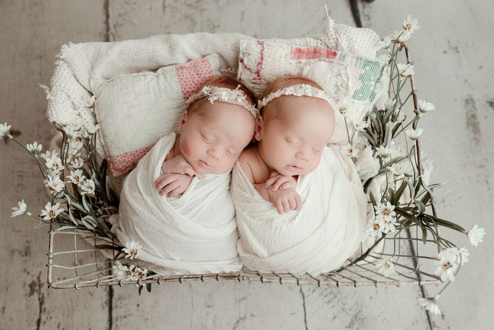 Minimalist newborn photography with white flowers and soft fabric on light backdrop.