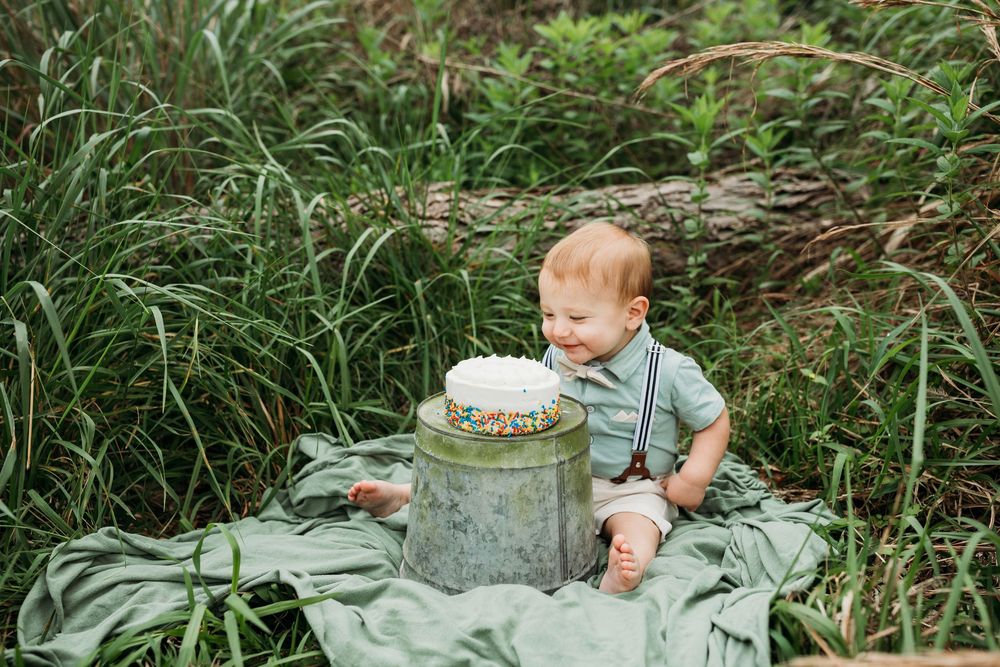 A small cake smash session in a lush green garden setting features a white cake on a gray blanket.