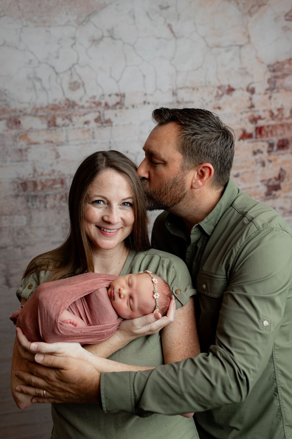 Indoor family photography session against exposed brick wall with soft natural lighting.