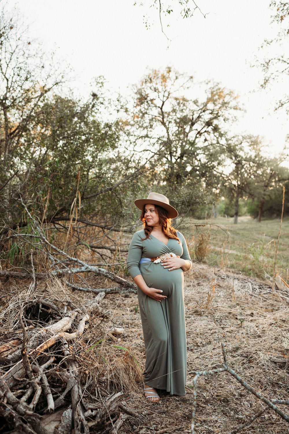 Maternity photos in nature showing expecting mother in sage green dress among fallen branches.