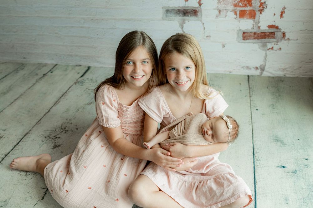 Studio portraits on white floor showing tender family moments in soft pink tones.