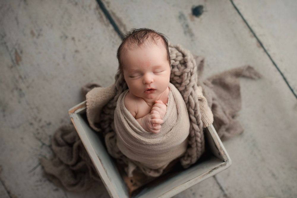 Artistic newborn photography with muted tones and textured floor setting.