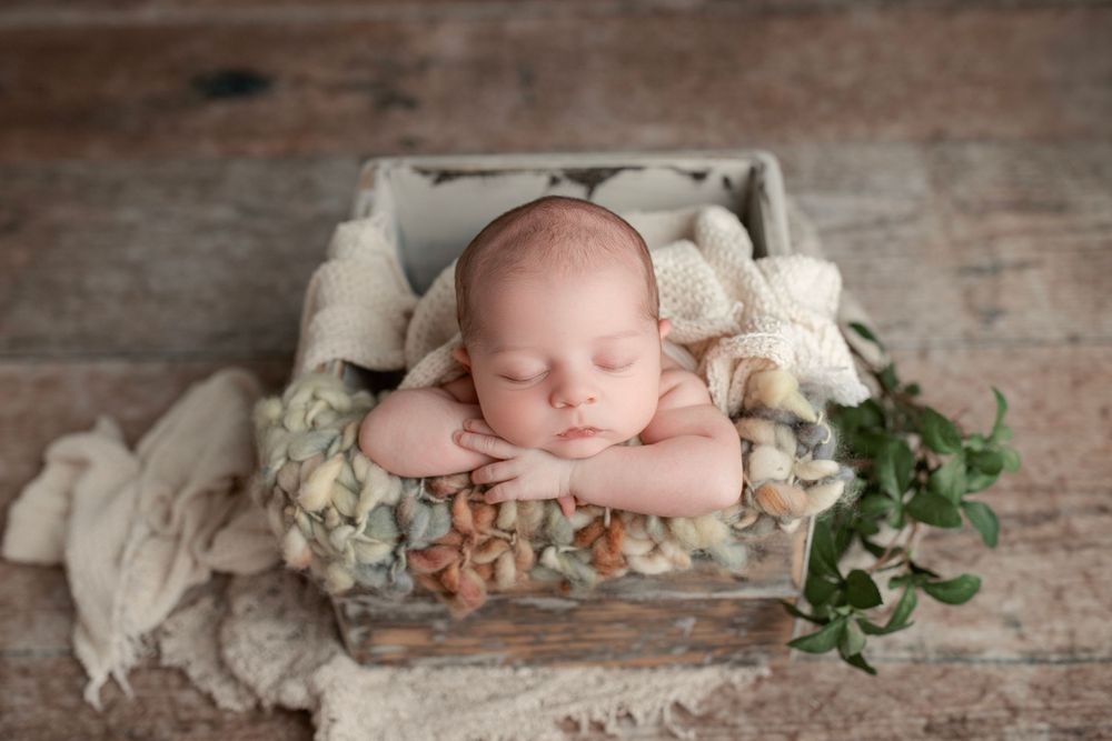 A series of artistic newborn photos with soft white fabrics and floral accents on a rustic wooden backdrop.