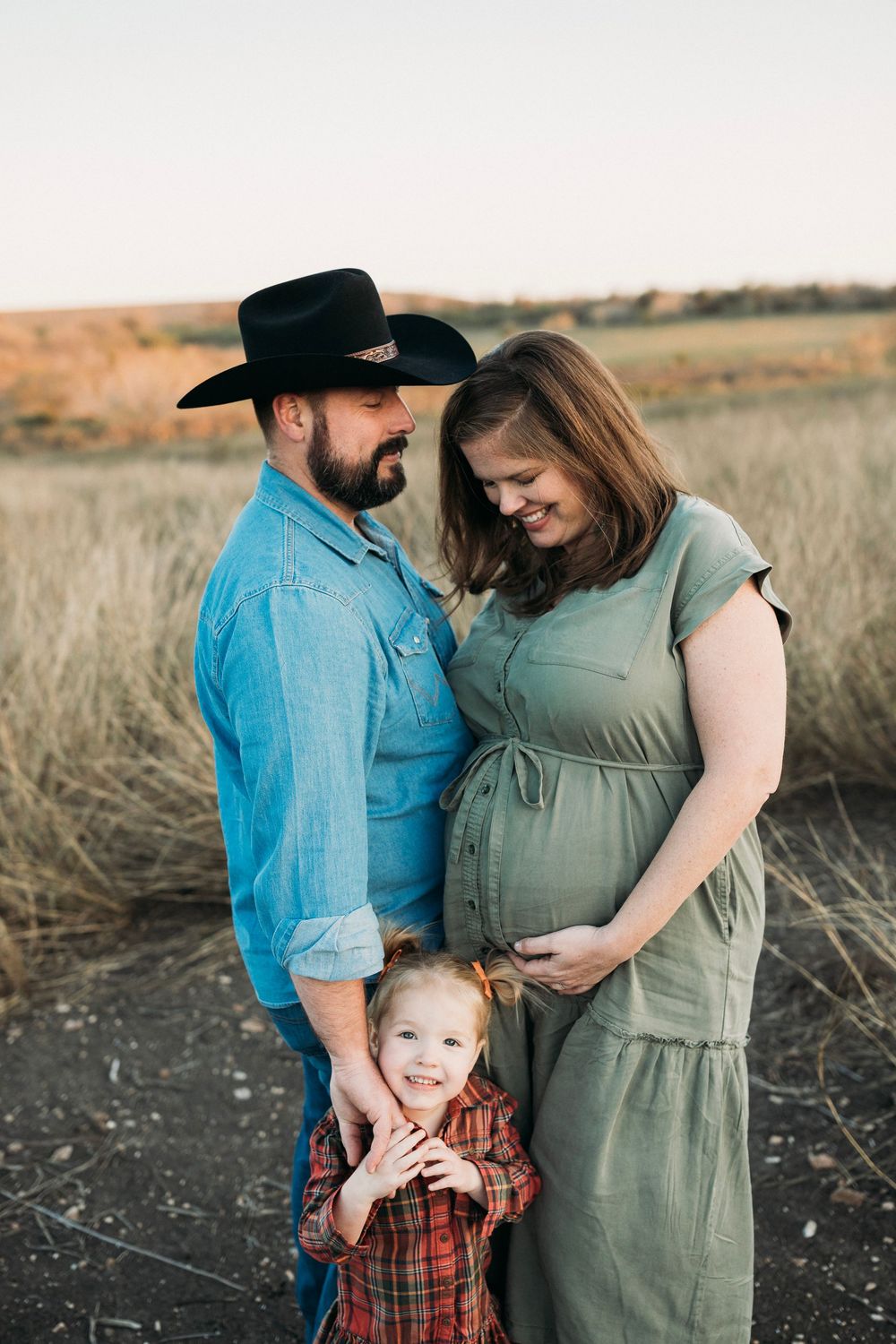 Sunset maternity photo session in a field with family wearing casual country attire.