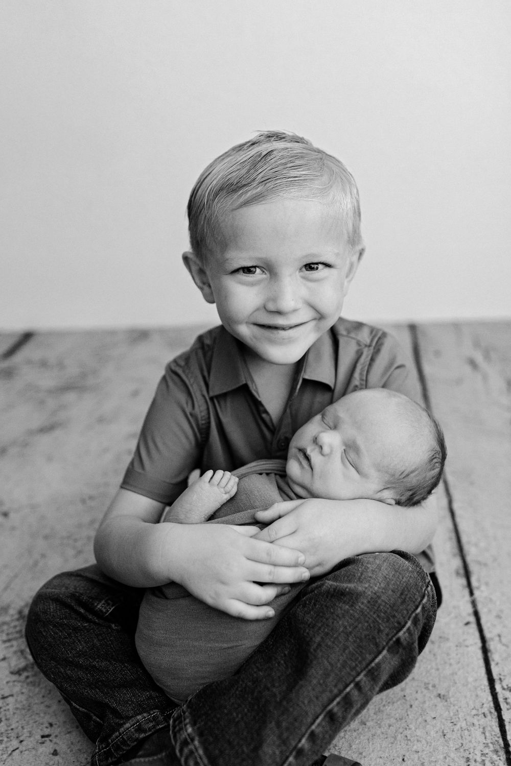 Two young children sitting on wooden floor during portrait session.