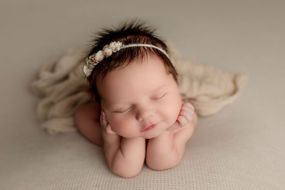Sleeping newborn with delicate headband resting head on hands in studio setting.