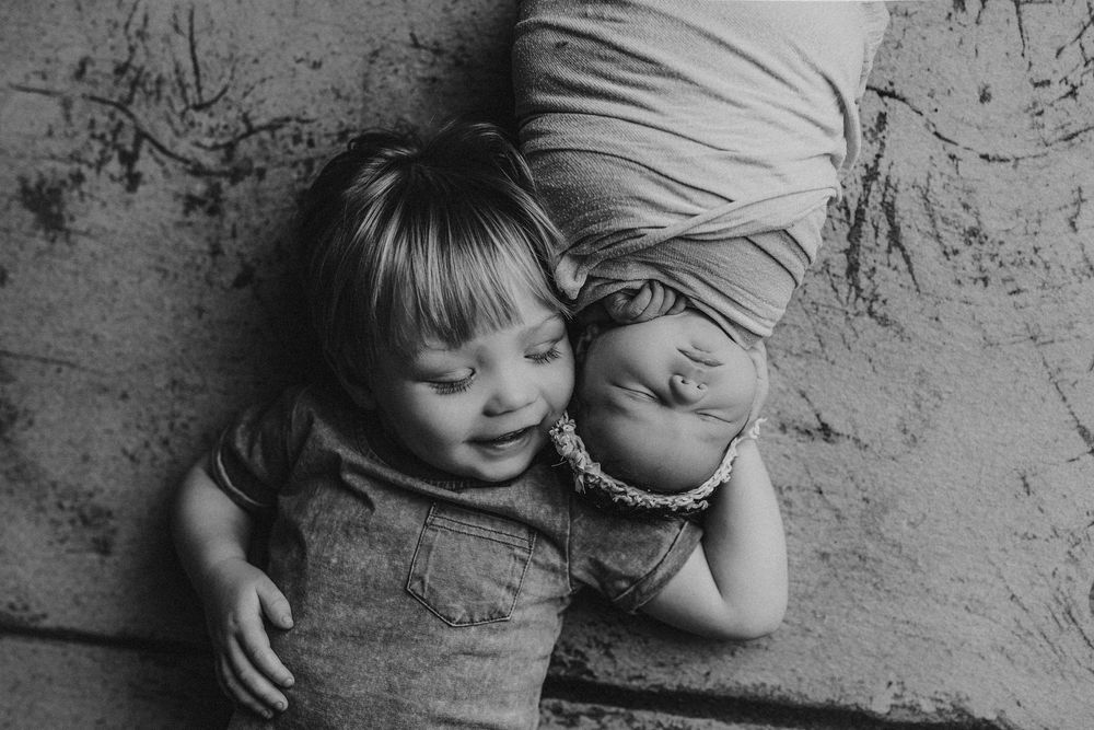 Black and white image of two children laying on textured floor.