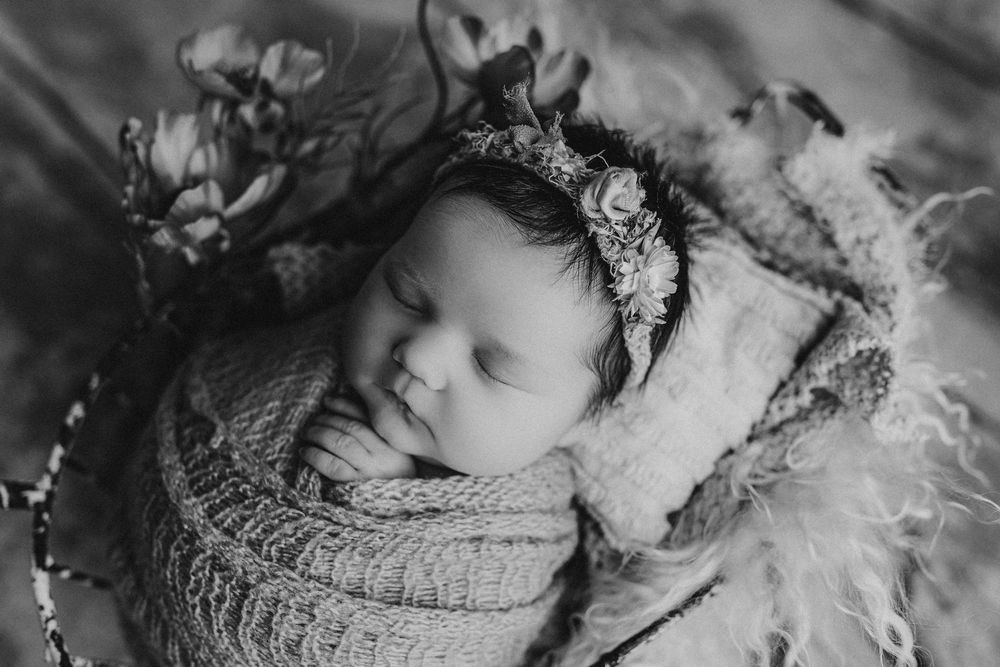 Black and white portrait of sleeping newborn in knit wrap and floral headband.