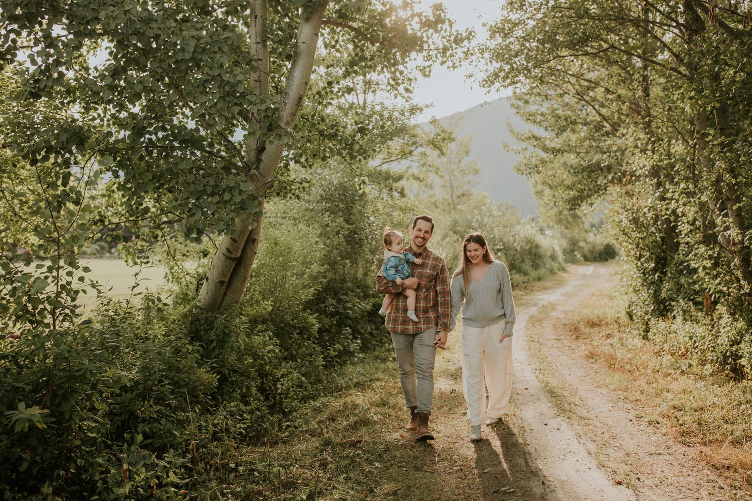 A couple walking on a trail near green lake, the man is holding their baby daughter.