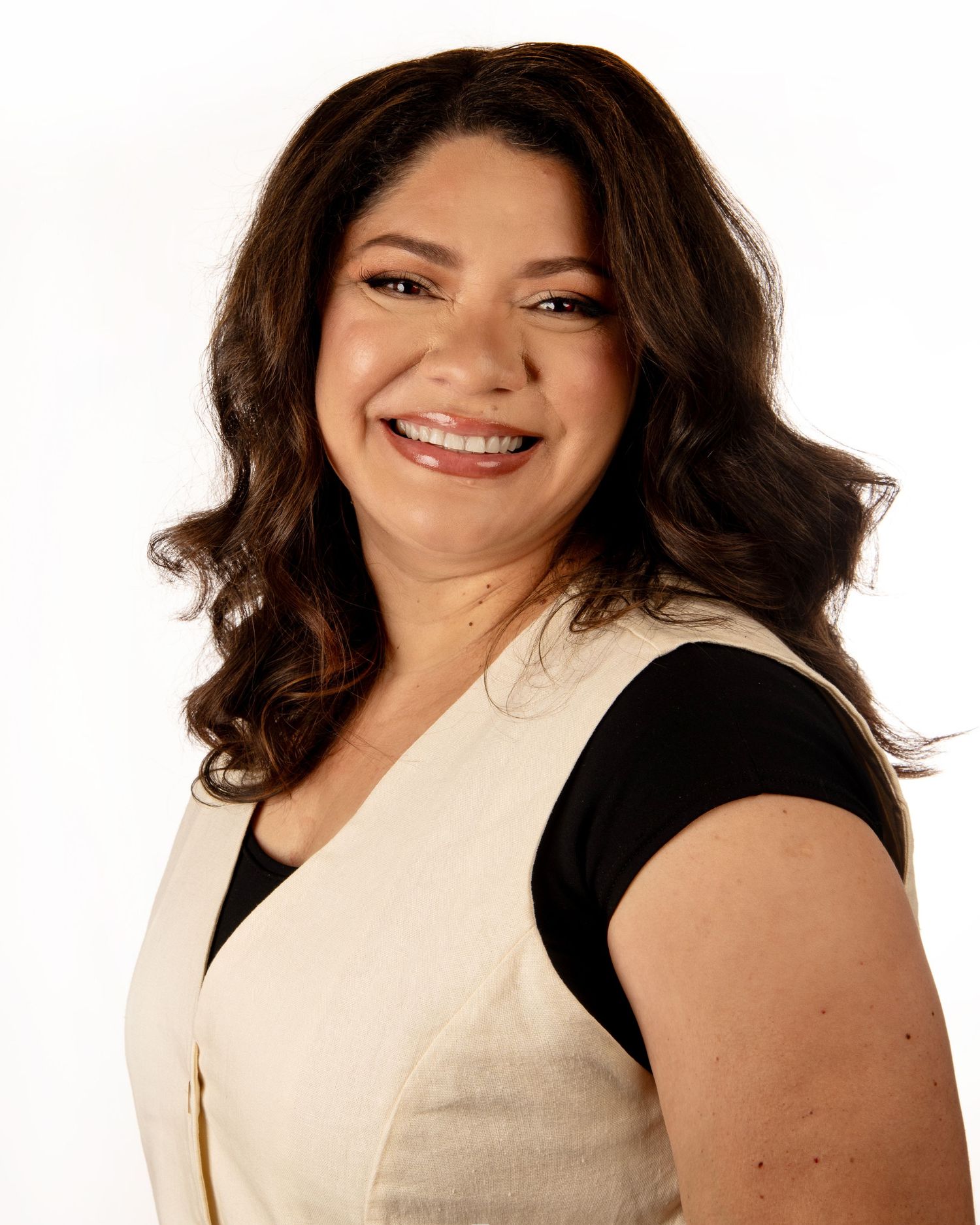 Professional headshot of a person wearing a black top and cream vest against white background.