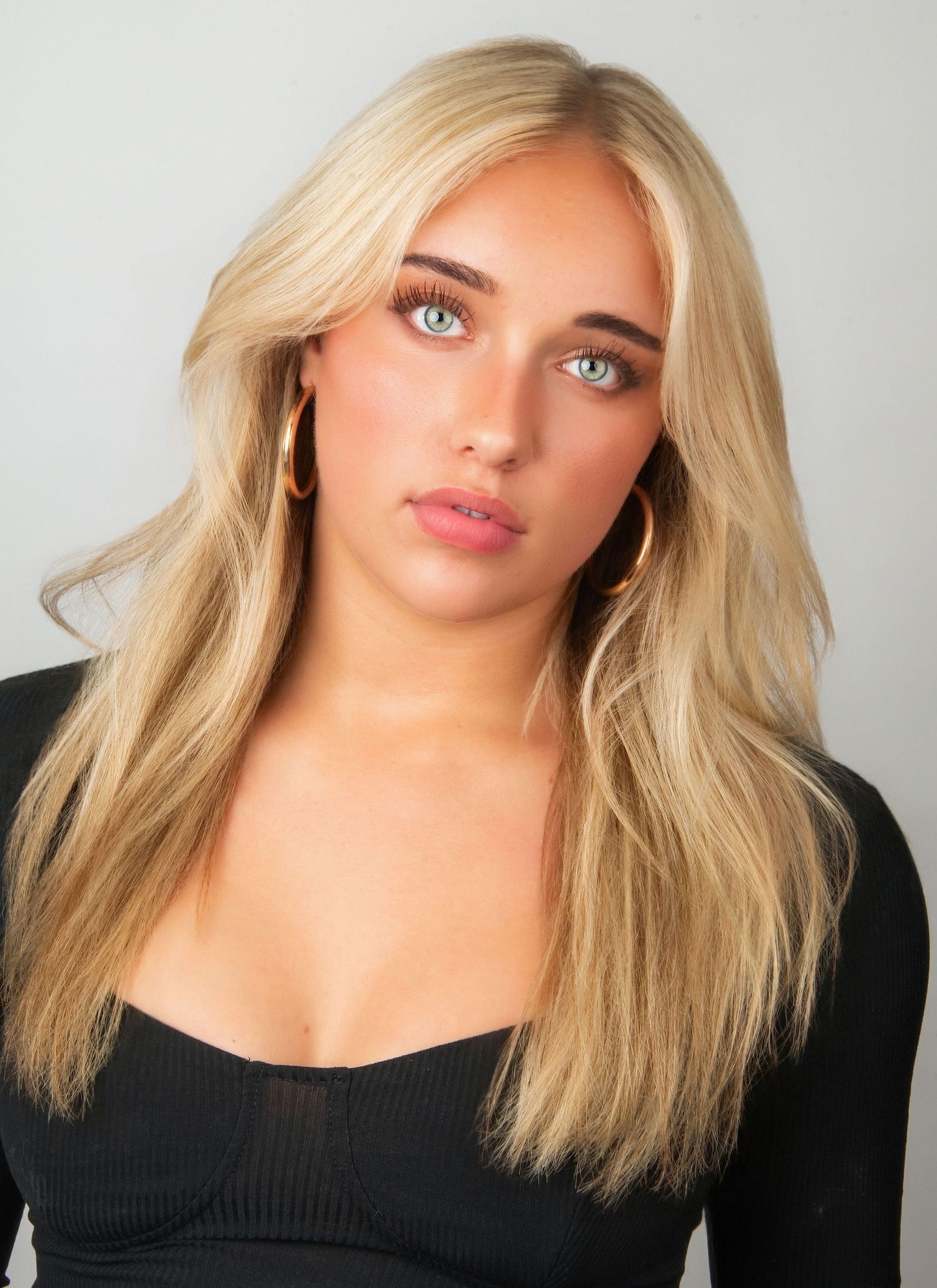 Young blonde woman with blue eyes wearing gold hoop earrings and black top, posing for a professional headshot photo.