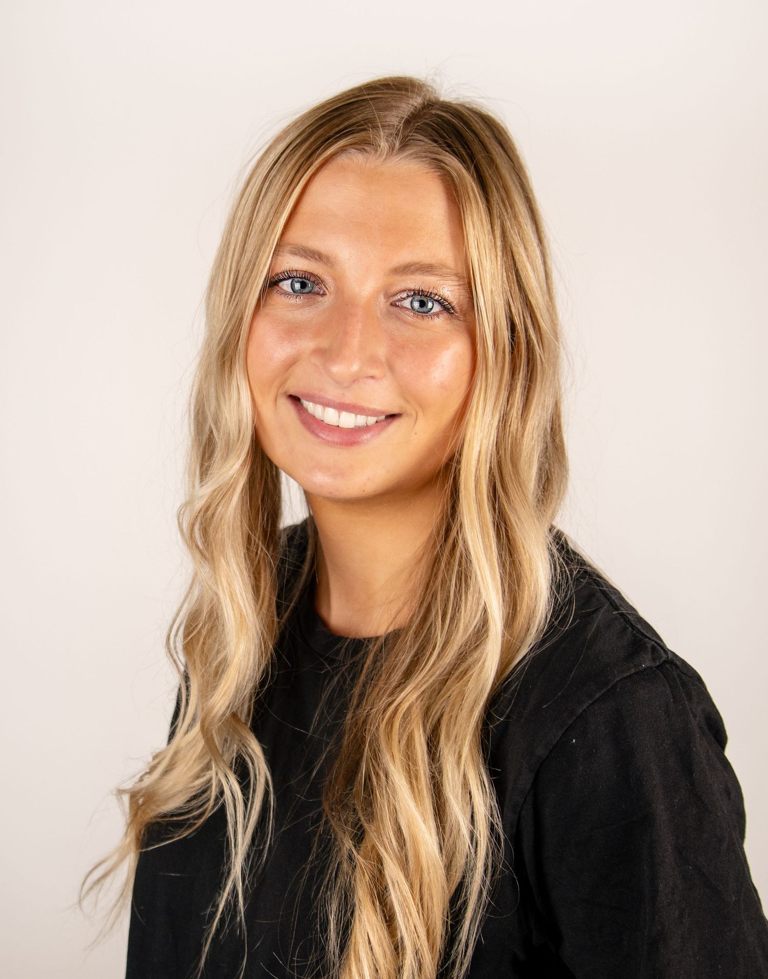 Portrait of someone with long blonde hair wearing a black top against a white background.