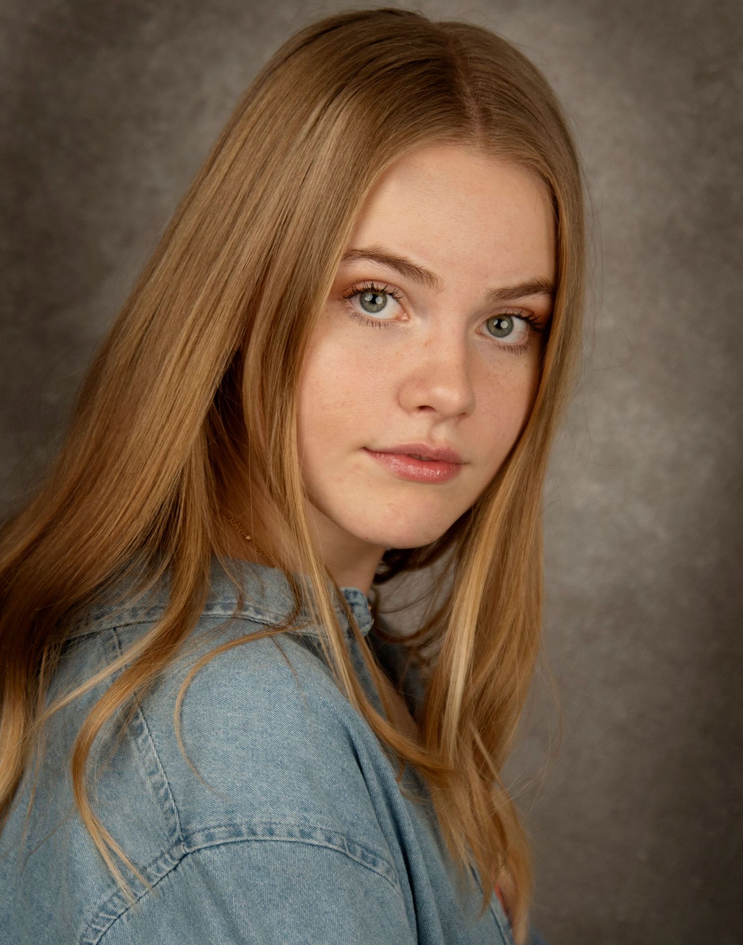 Portrait of a person with long blonde hair wearing a denim jacket against a muted background.