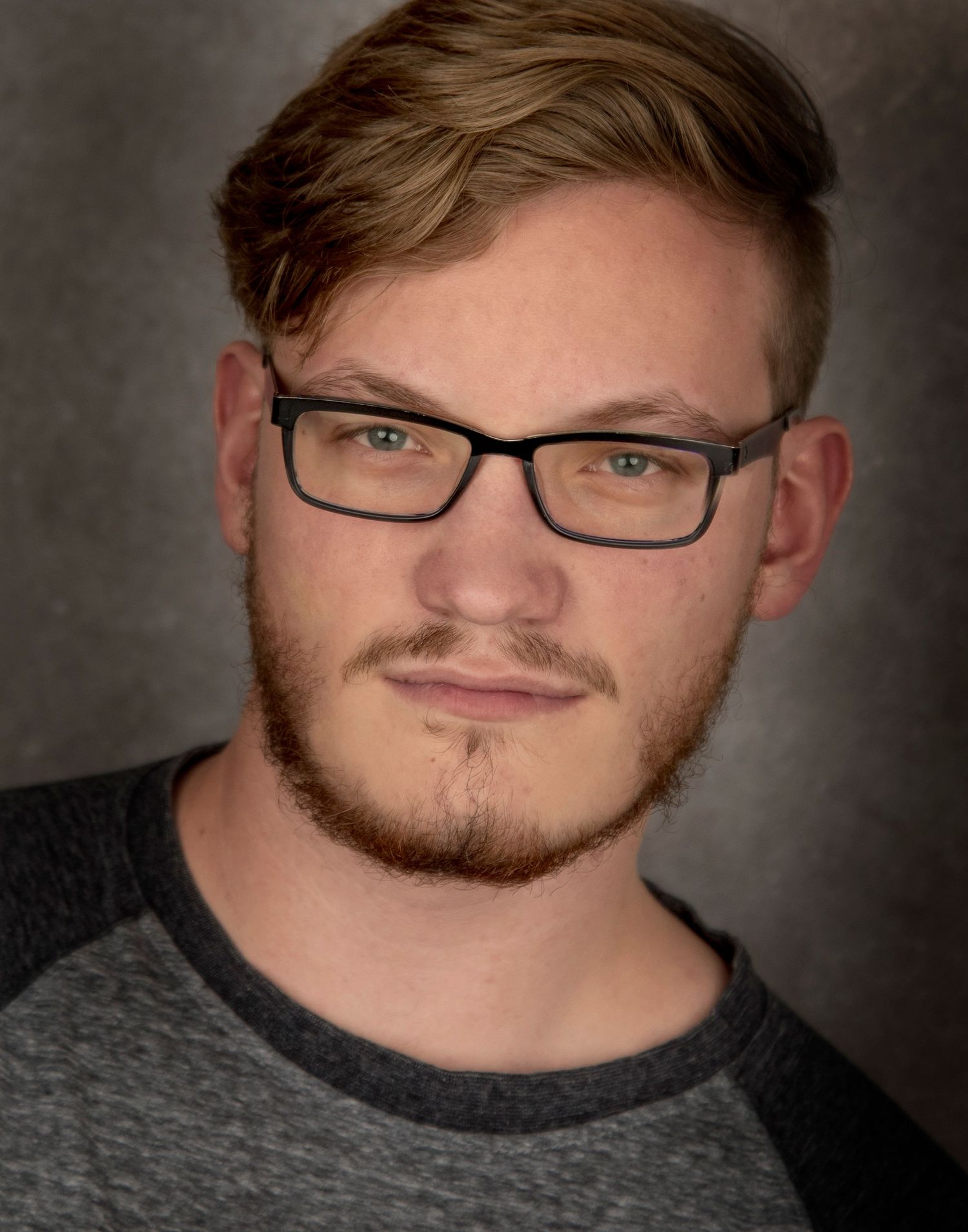 Professional headshot of a person wearing glasses and a dark shirt against a textured background.