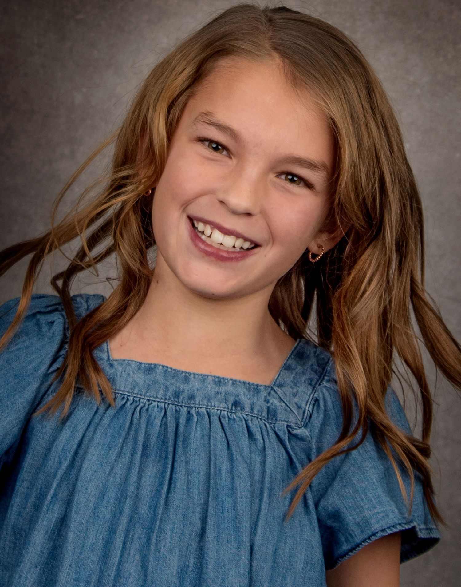 Portrait of a young person in a blue denim top with flowing brown hair against a textured background.