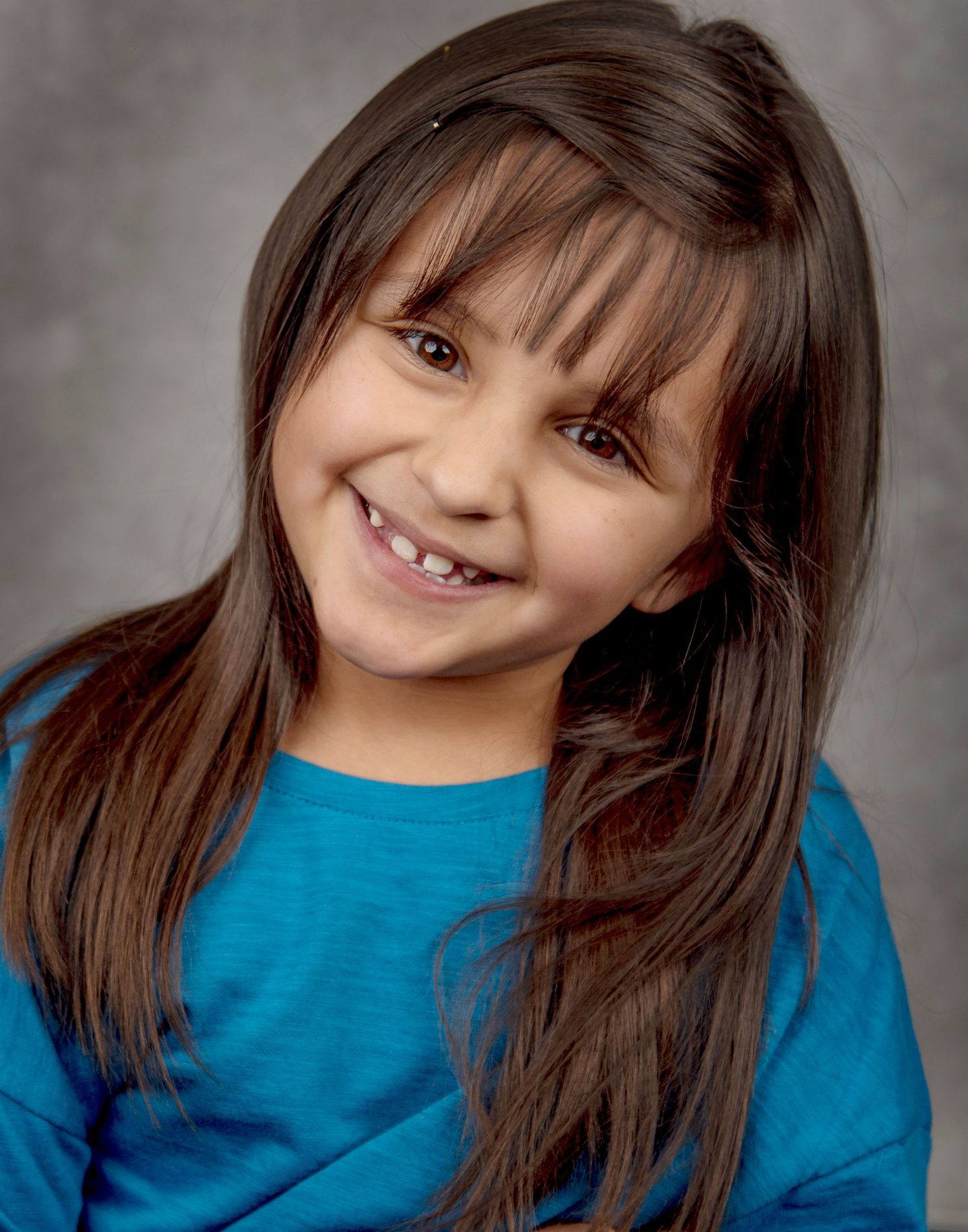 Child in a bright blue top poses for portrait photo with a cheerful expression and straight dark hair with bangs.