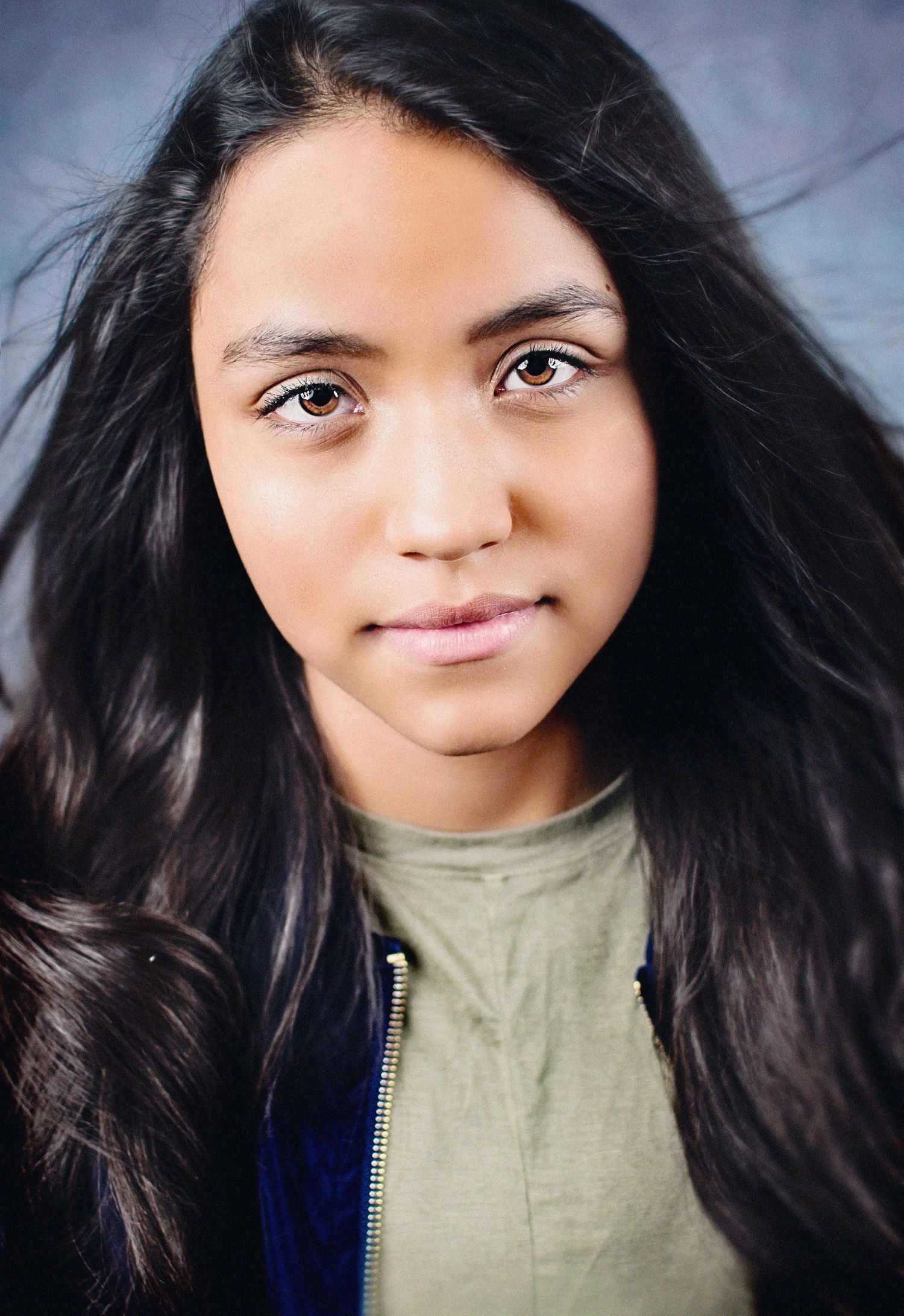 Close up portrait of a person with long dark hair wearing a green top and blue jacket.