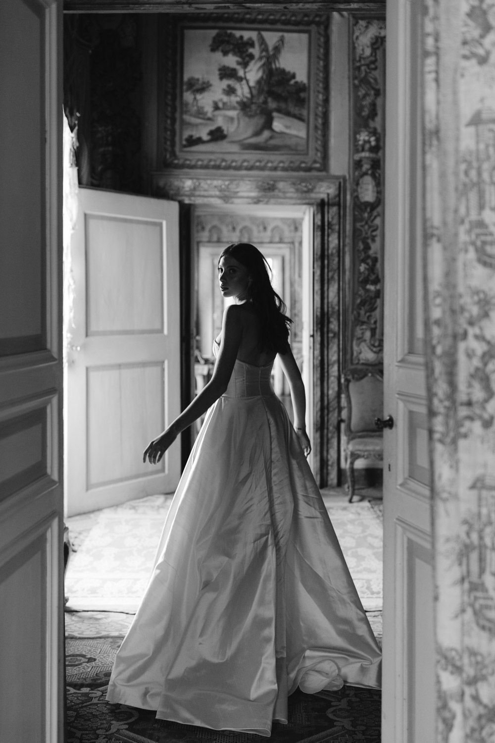 Artistic black and white silhouette of flowing gown in an ornate interior hallway.
