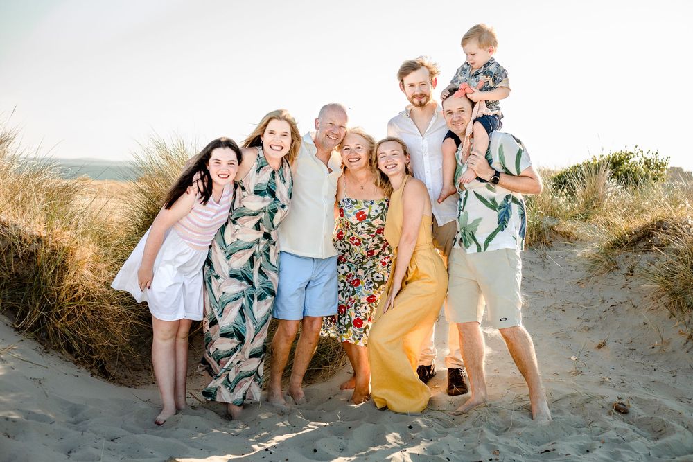 On a sunset beach on Hayling Island, Hampshire, a family stand in the sand hugging together and smiling during their photoshoot.