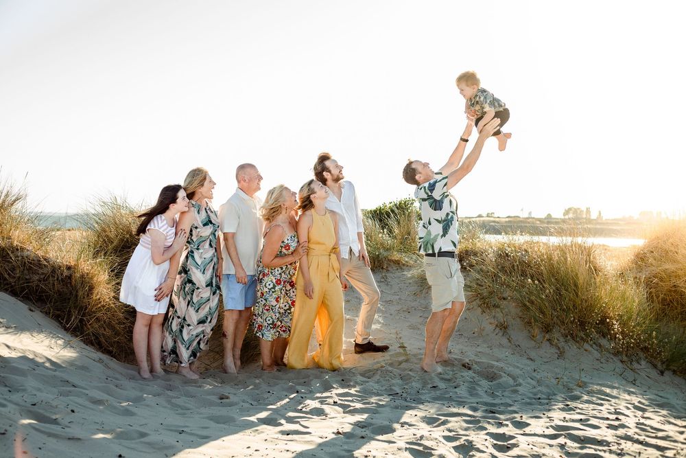 On a sunset beach on Hayling Island, a family stand in the sand hugging, watching at the toddler of the family thrown in the air.