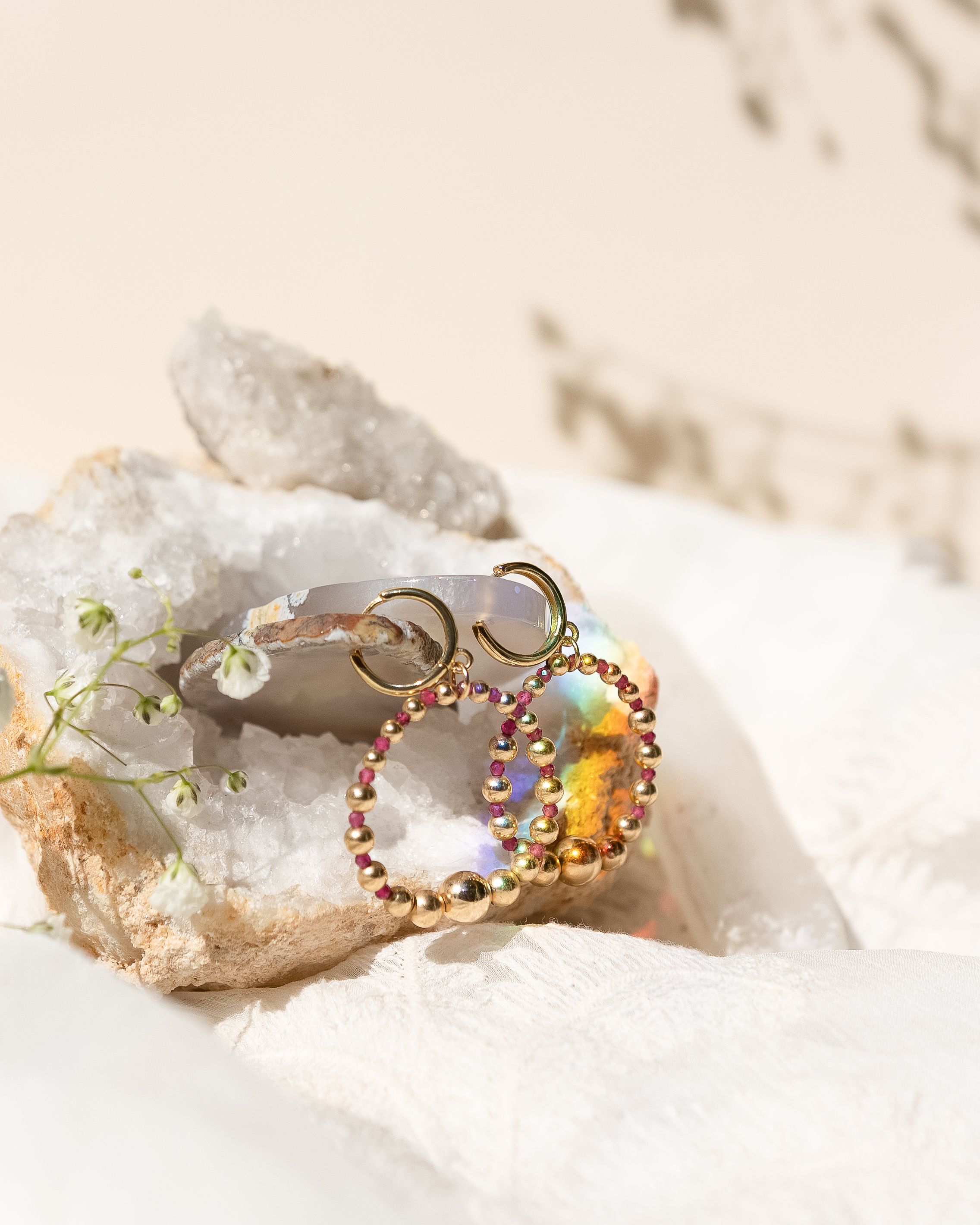 Jewelry display featuring a colorful crystal charm on white crystal geode backdrop with delicate flowers.