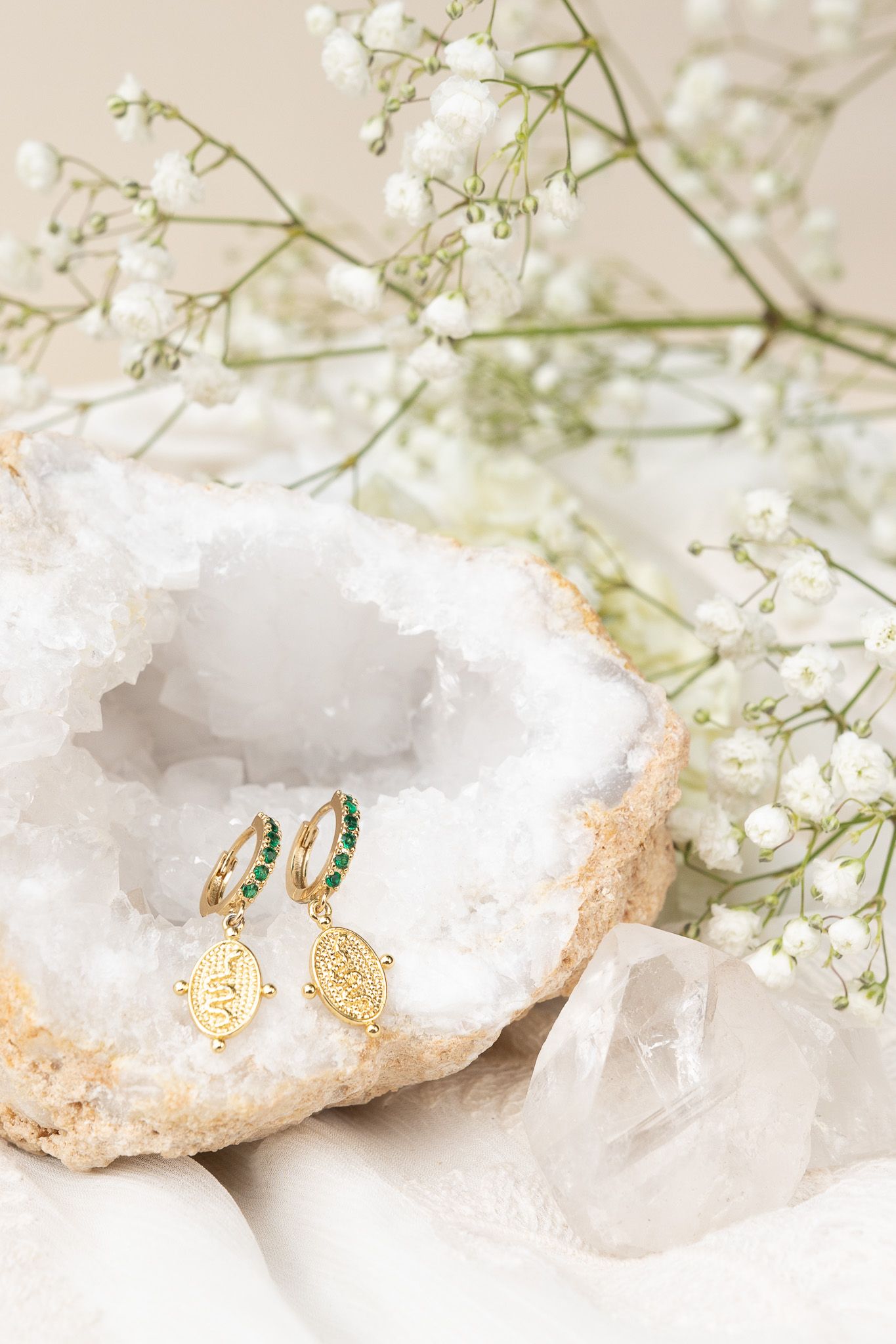Ornate gold earrings displayed in white crystal geode with delicate baby's breath flowers.