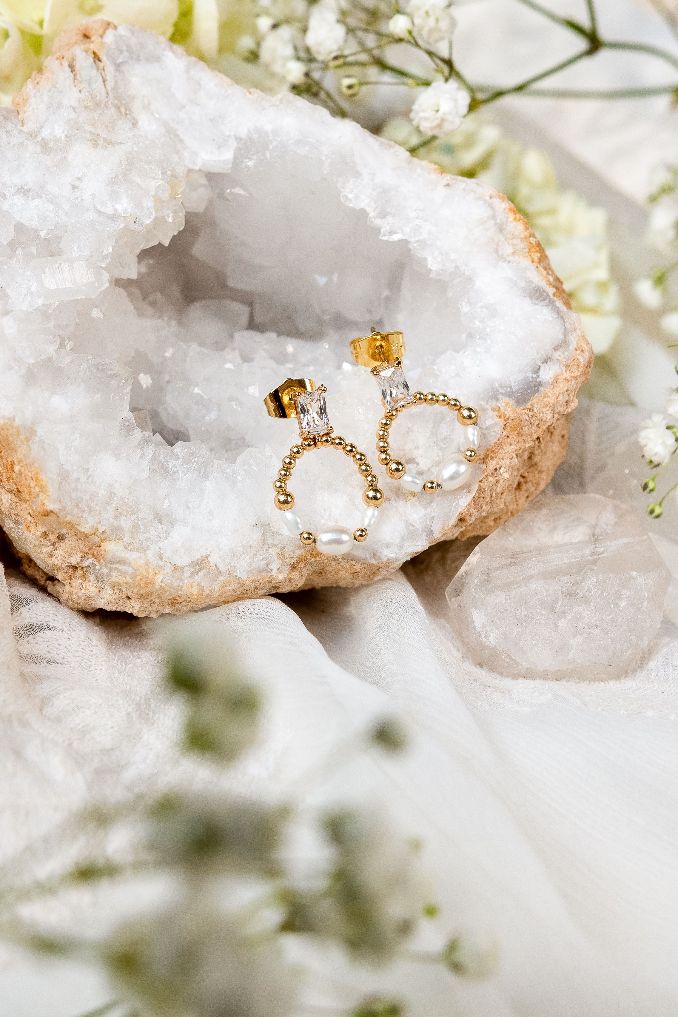 Pearl and gold earrings displayed on a white crystal geode surface with delicate floral accents.