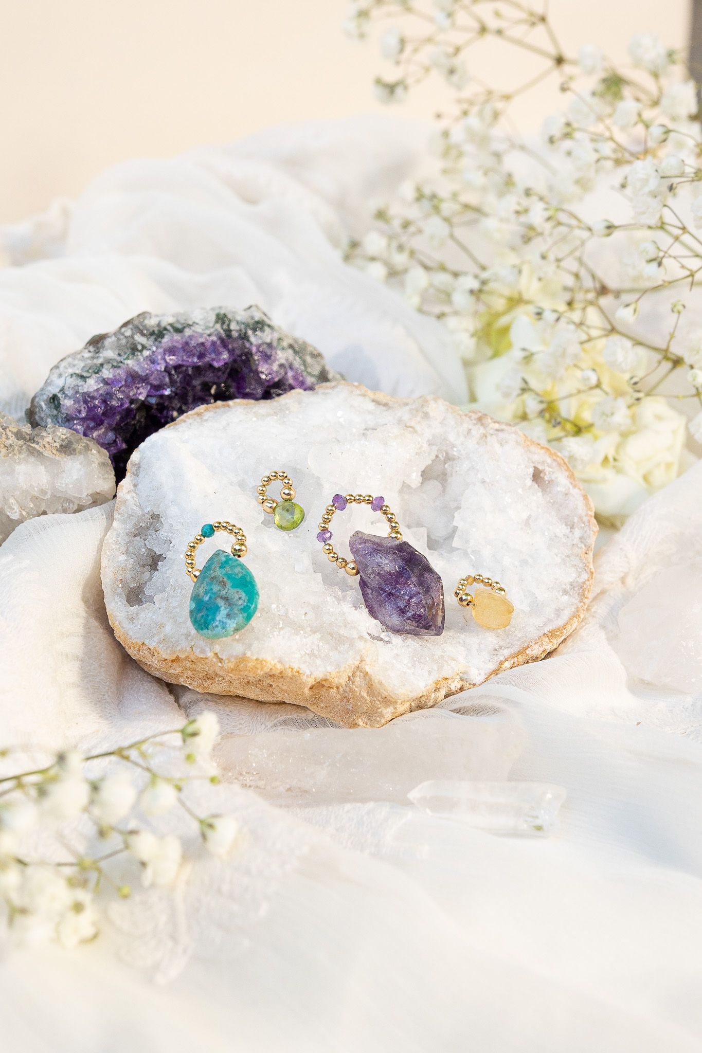 Colorful gemstone jewelry arranged on white crystal geode with amethyst and baby's breath accents.