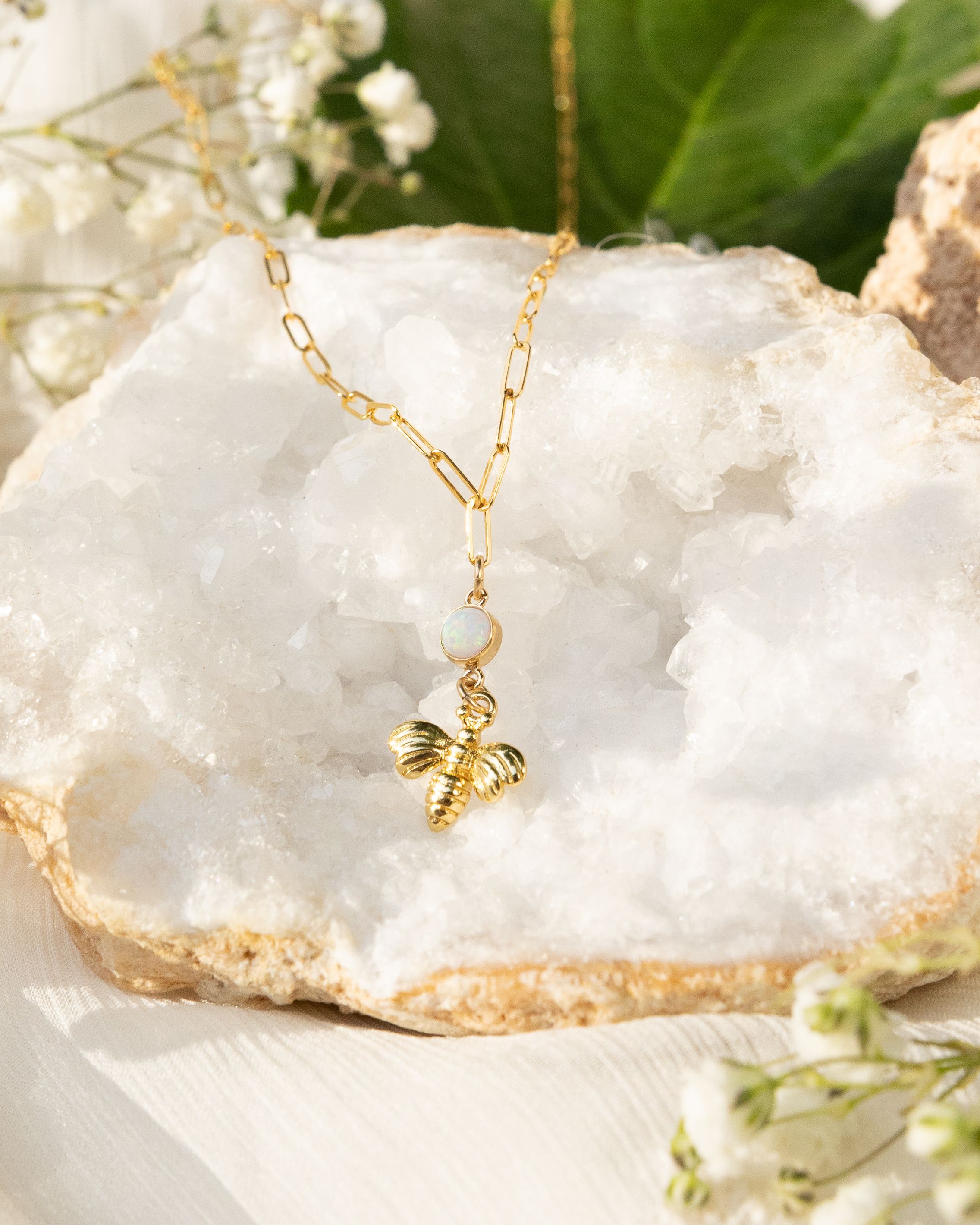 Gold butterfly pendant necklace displayed on white crystal geode with baby's breath flowers.