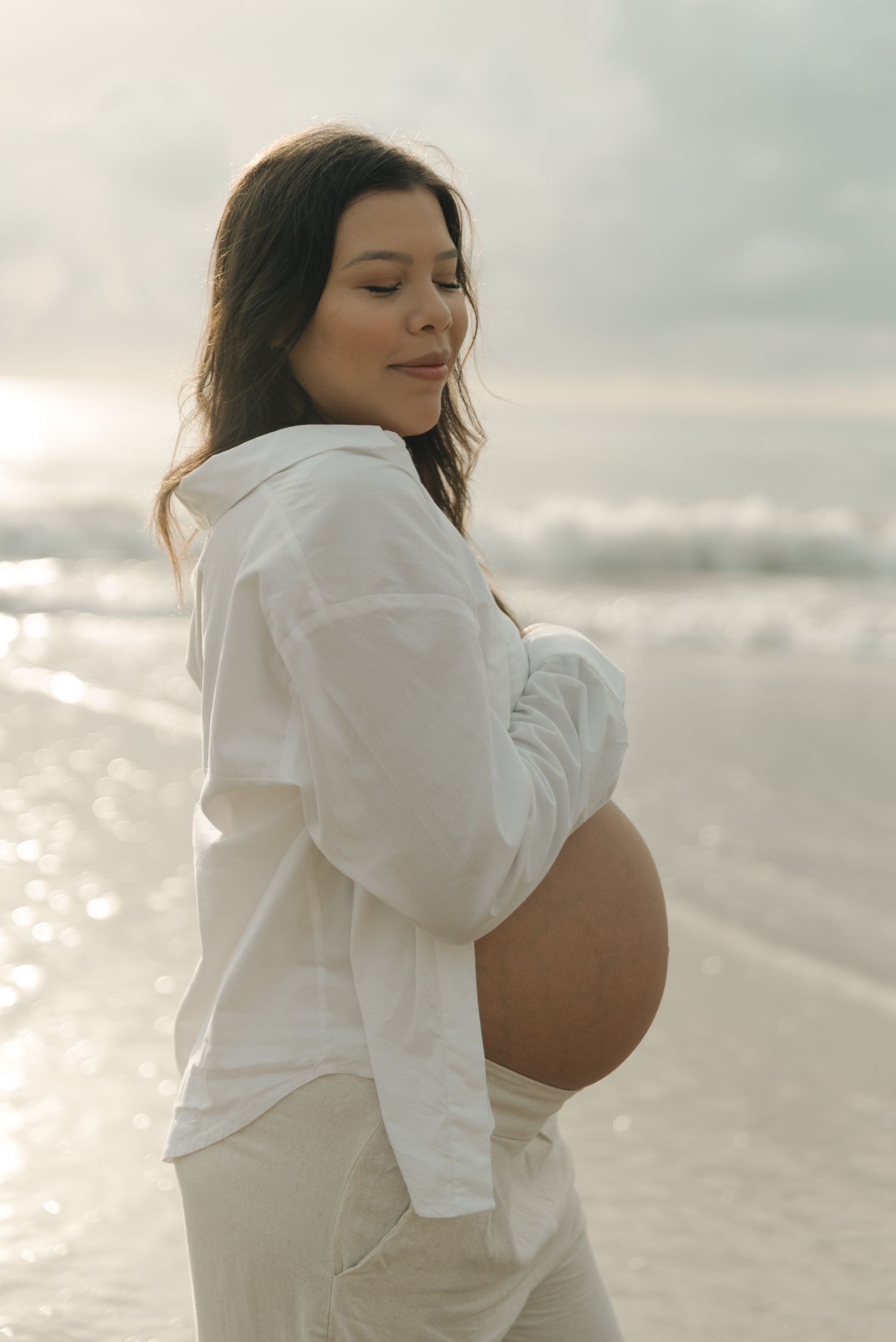 Serene beach maternity photo with woman in white clothing at sunset.