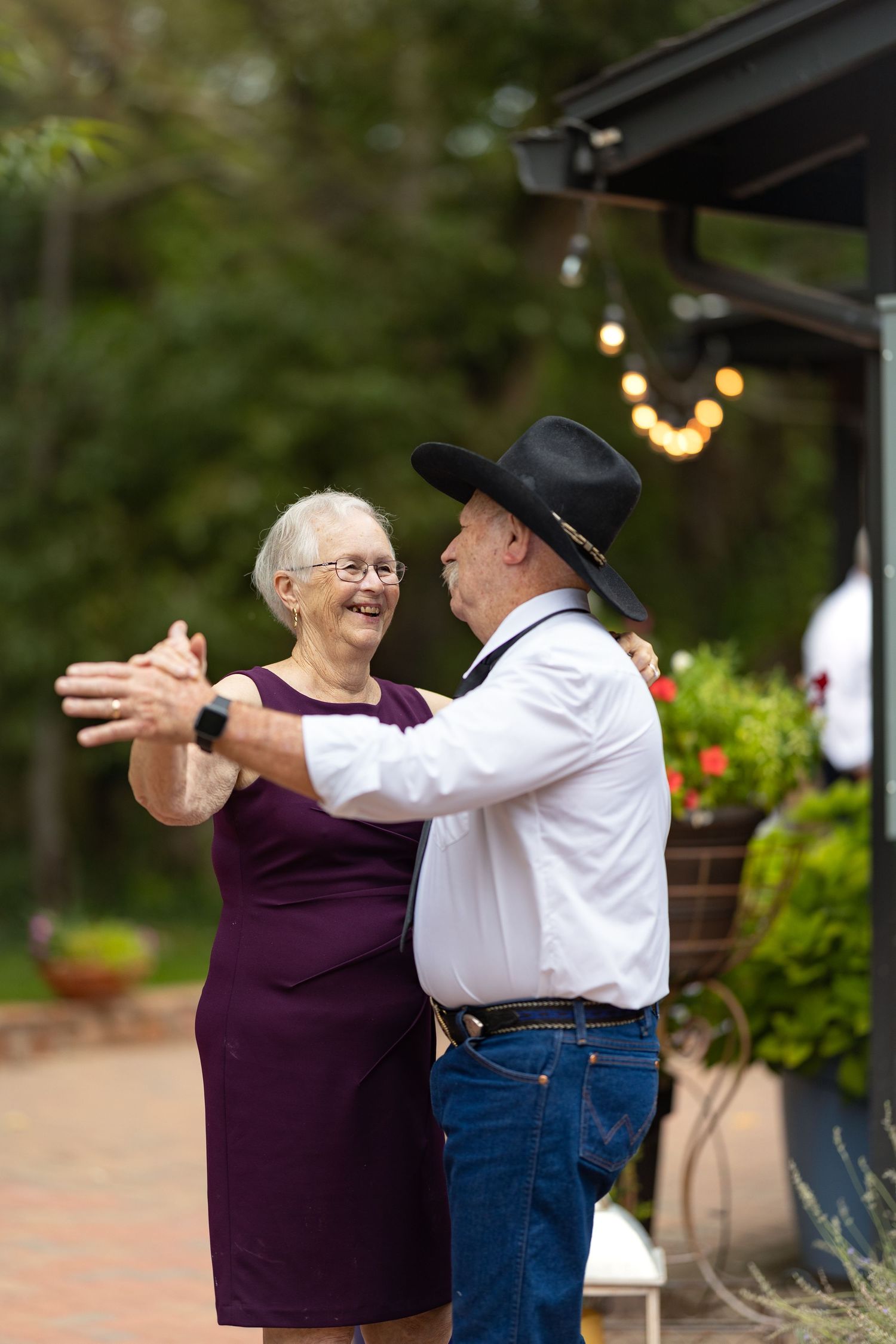 A dancing couple shares a joyful moment at an outdoor venue with string lights in the background.