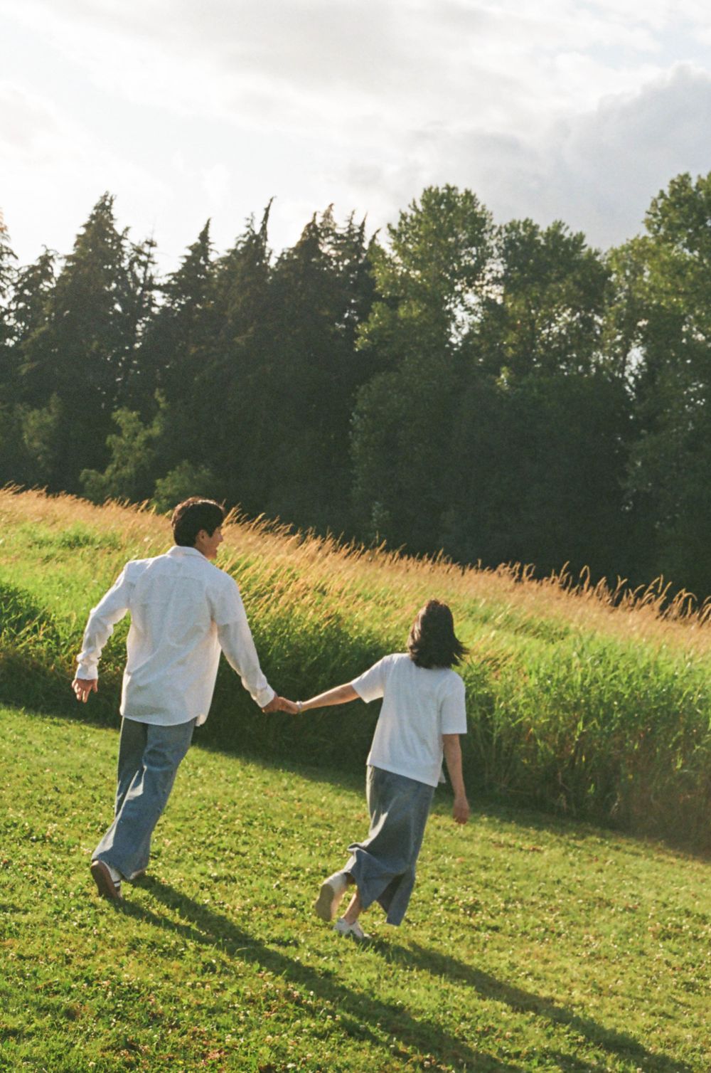 Two people run playfully through a green field at sunset.