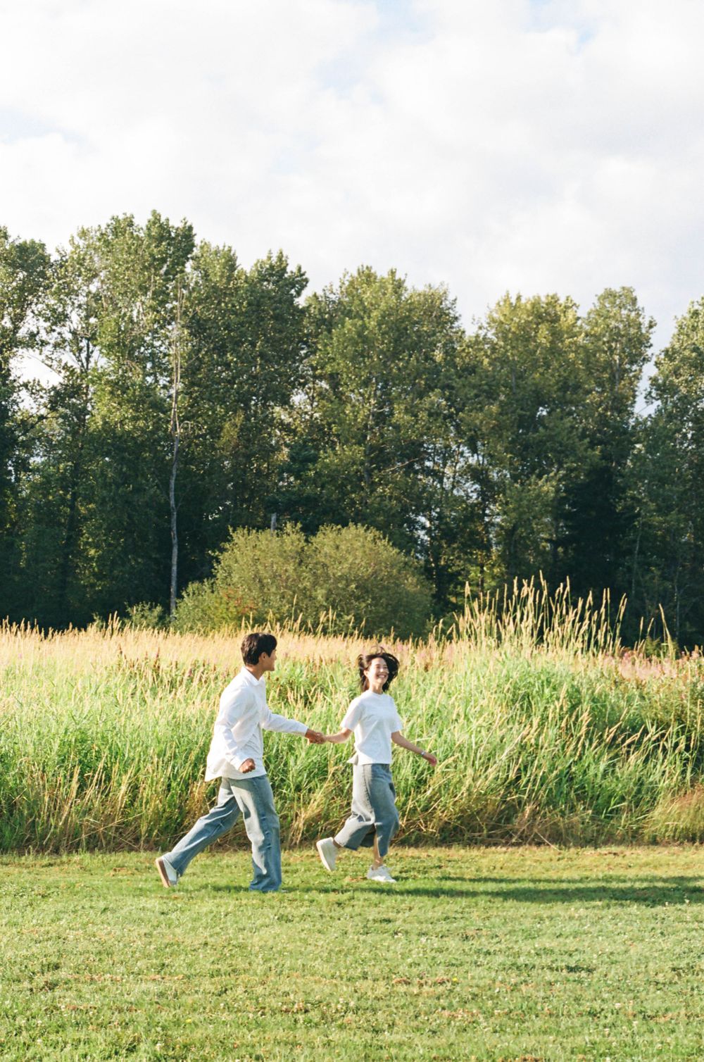 People dancing and moving freely in a sunlit meadow bordered by tall grass and trees.