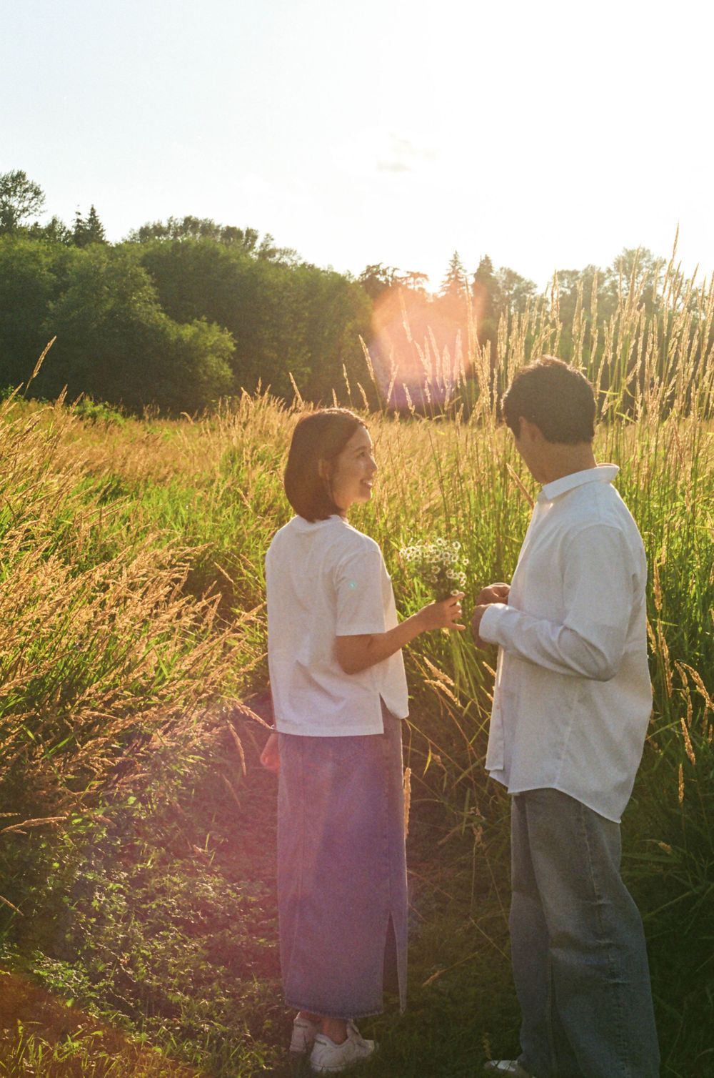 Two people stand together among golden grass at sunset, creating a romantic silhouette.