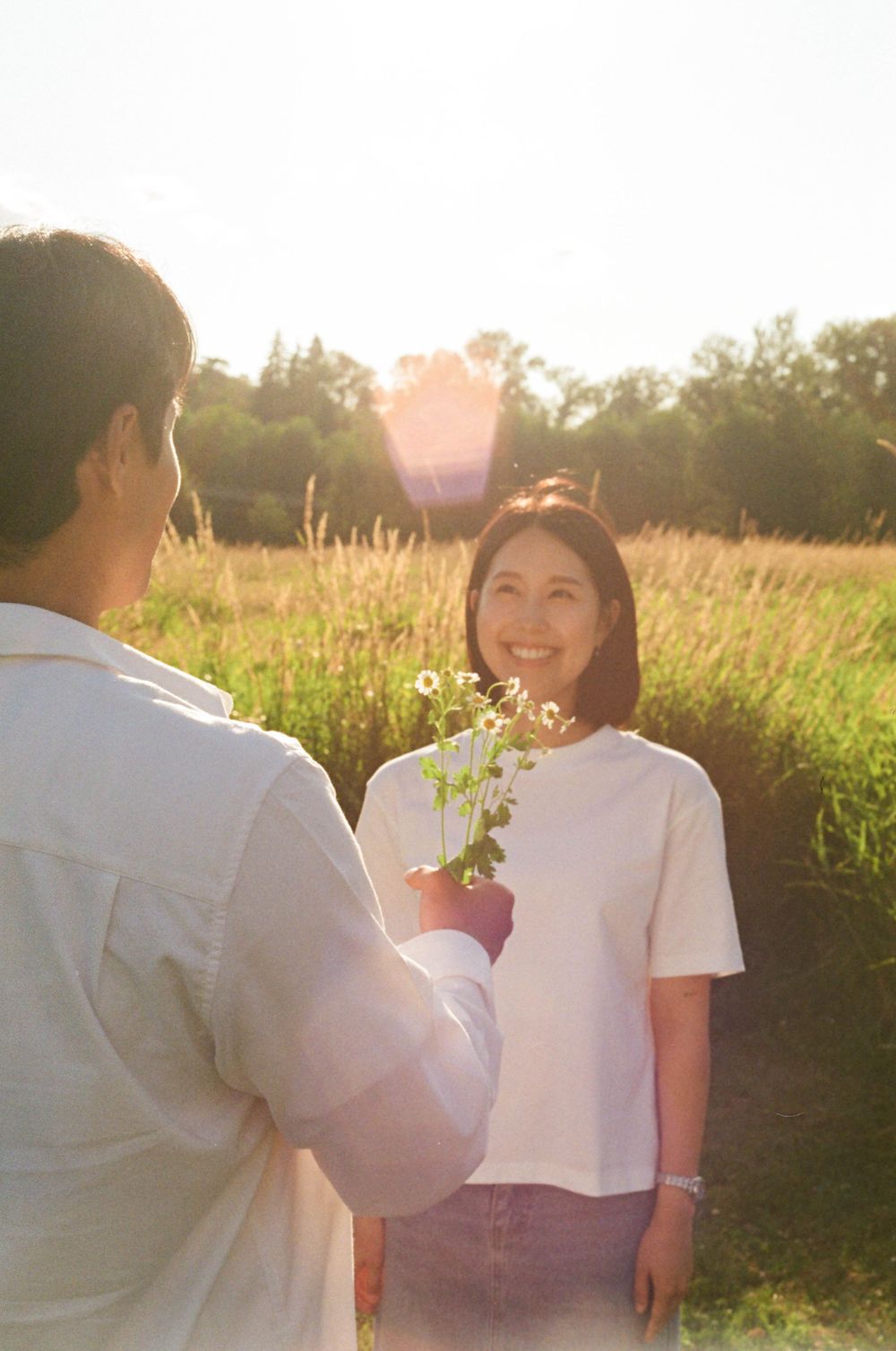 A couple shares a joyful moment together in a meadow during sunset.
