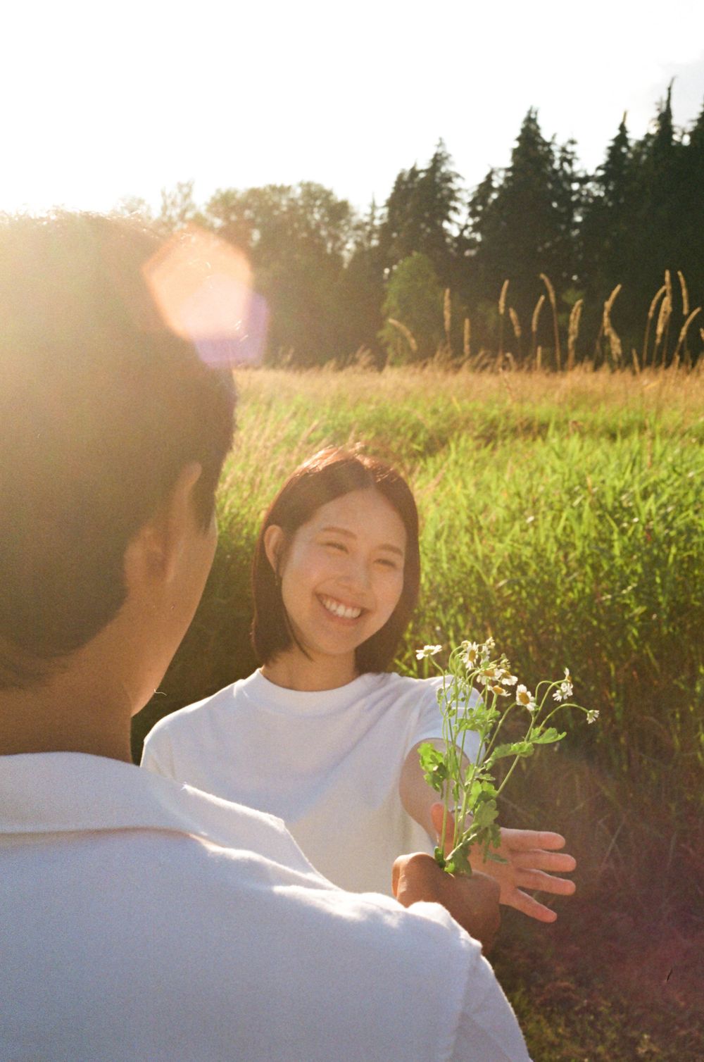 A tender moment between a couple holding flowers in a summer field at dusk.
