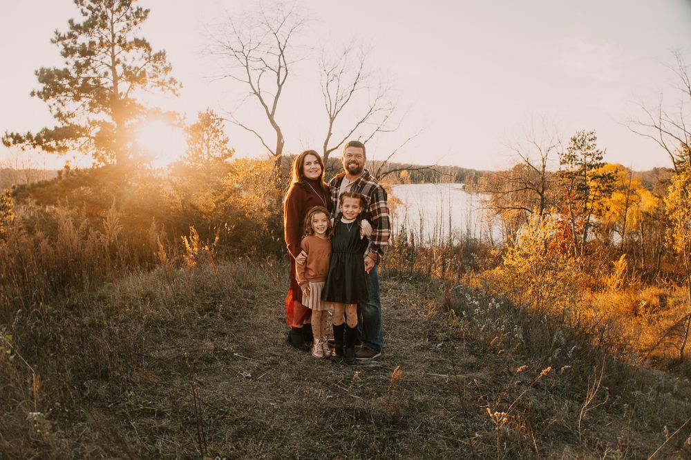 Group stands together in a golden sunset field with tall grass and trees creating a warm autumn atmosphere.
