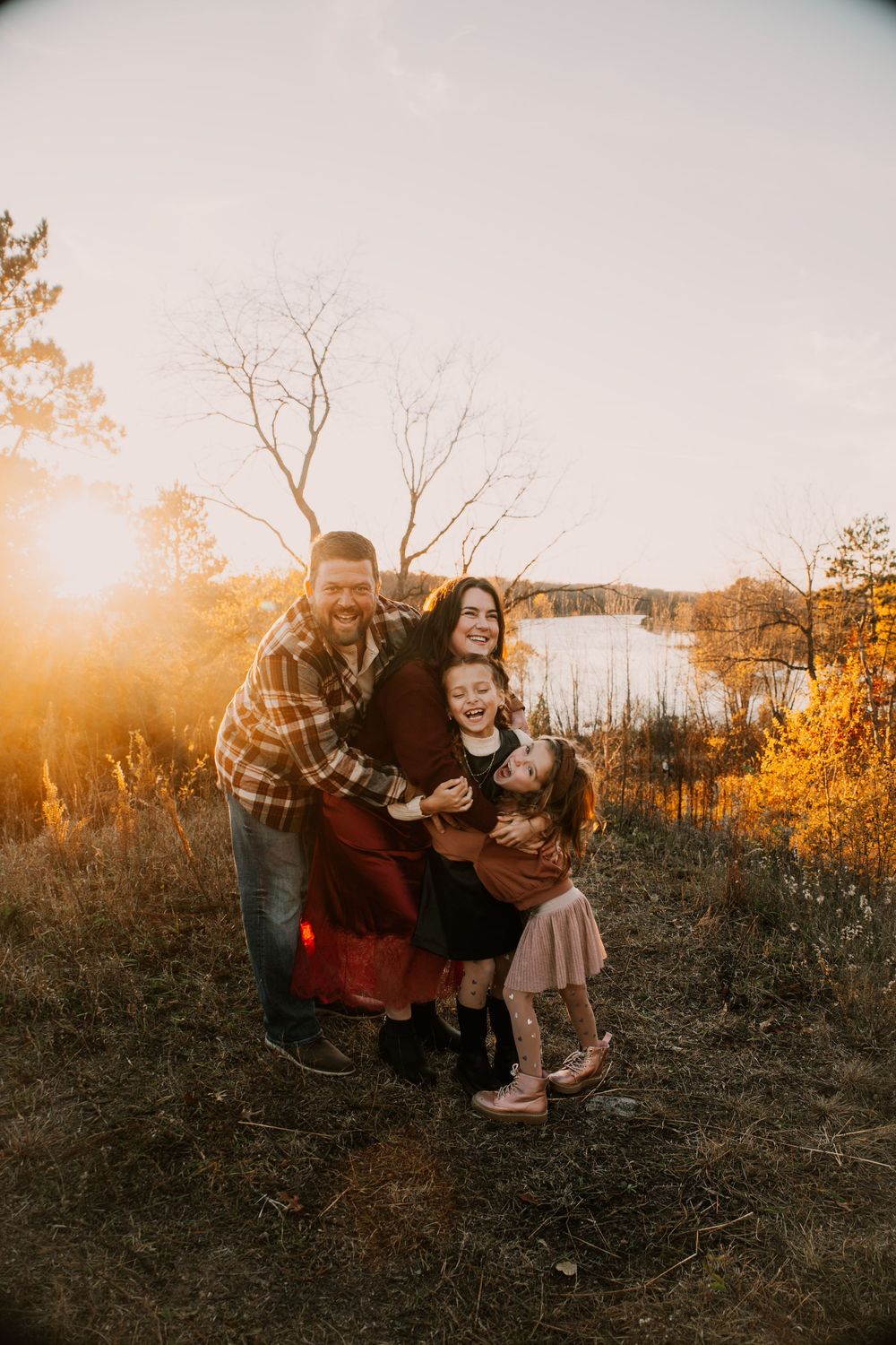 A family shares a playful moment together during golden hour by a scenic lake with fall colors.